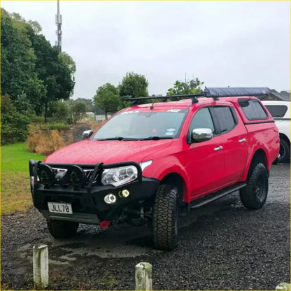 Red mitsubishi triton pickup with black roof rack and front bumper featuring gt hoop bullbar and rock sliders